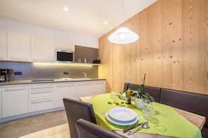 Une cuisine moderne avec des meubles blancs, un four à micro-ondes et un évier. On y trouve une table à manger recouverte d’une nappe verte, ainsi que des assiettes et une bouteille de vin.