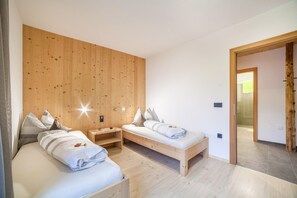 Une chambre avec deux lits, des murs recouverts de panneaux de bois et une porte visible donnant sur une autre pièce.
