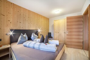 A bedroom with a bed, pillows, a nightstand, a chair, and wooden wardrobes.