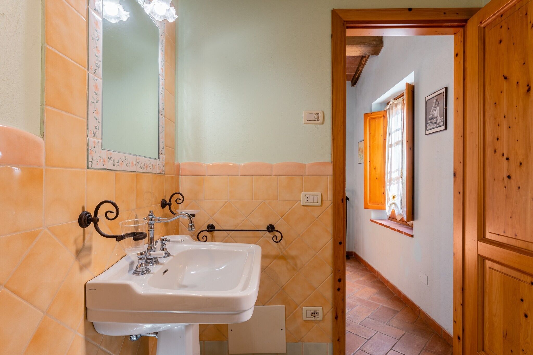 Un baño con lavamanos blanco, espejo y paredes de azulejos naranjas.
