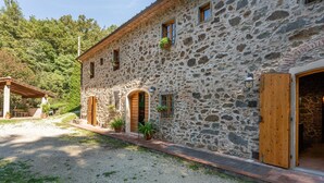 A stone building with a wooden door, a covered outdoor seating area, and potted plants. - Holiday Home "Mulino di Beboli" with Pool & Garden (Lamporecchio (PT))