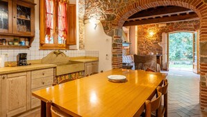 A stone-walled kitchen with a wooden table and chairs, a window with curtains, and a view of the outdoors. - Holiday Home "Mulino di Beboli" with Pool & Garden (Lamporecchio (PT))