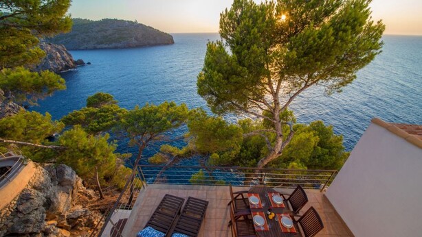 Une terrasse avec une table et des chaises, donnant sur une zone côtière bordée d’arbres et sur la mer.