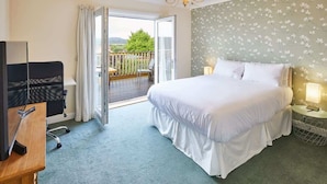 Ein Hotelzimmer mit Bett, Schreibtisch, Stuhl, Fernseher, Lampe und einem Balkon mit Blick.