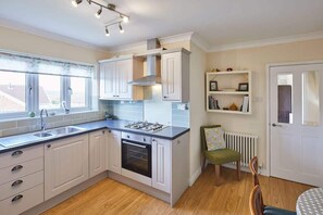 A kitchen with white cabinets, a gas stove, and a window with a view. - Host & Stay | Coach Cottage (Saltburn-by-the-Sea)