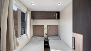 A compact room with two beds, a window, and a built-in cabinet. - "Mobile Home Next 229" with Pool, Garden & Wi-Fi (Pietra Ligure)