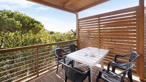 A covered outdoor area with a table and chairs, surrounded by a wooden fence and a view of greenery. - 'Mobile Home Alloro 165' with Pool, Private Terrace & Wi-Fi (Pietra Ligure)