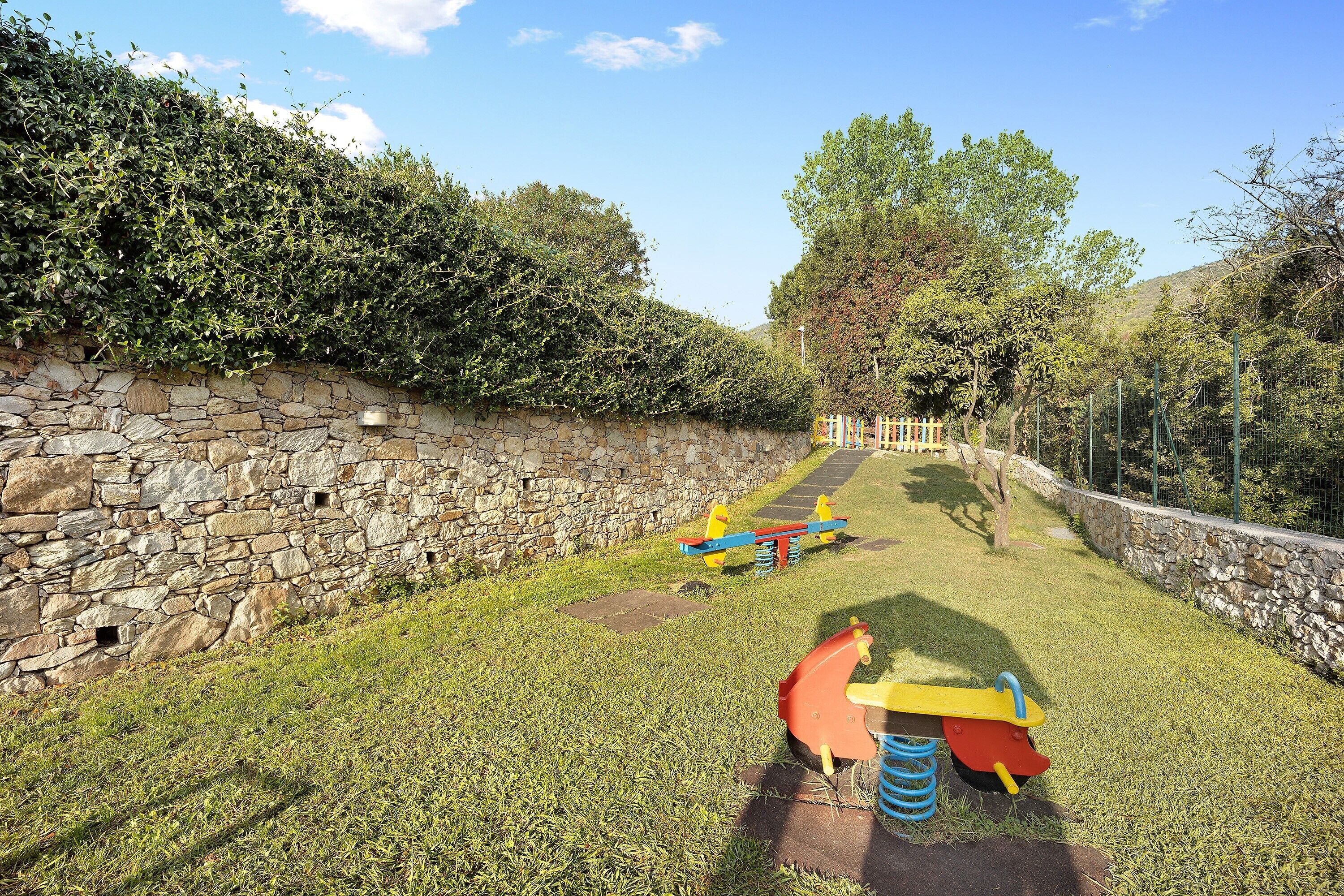 A stone wall, a grassy area with playground equipment, and trees in the background.