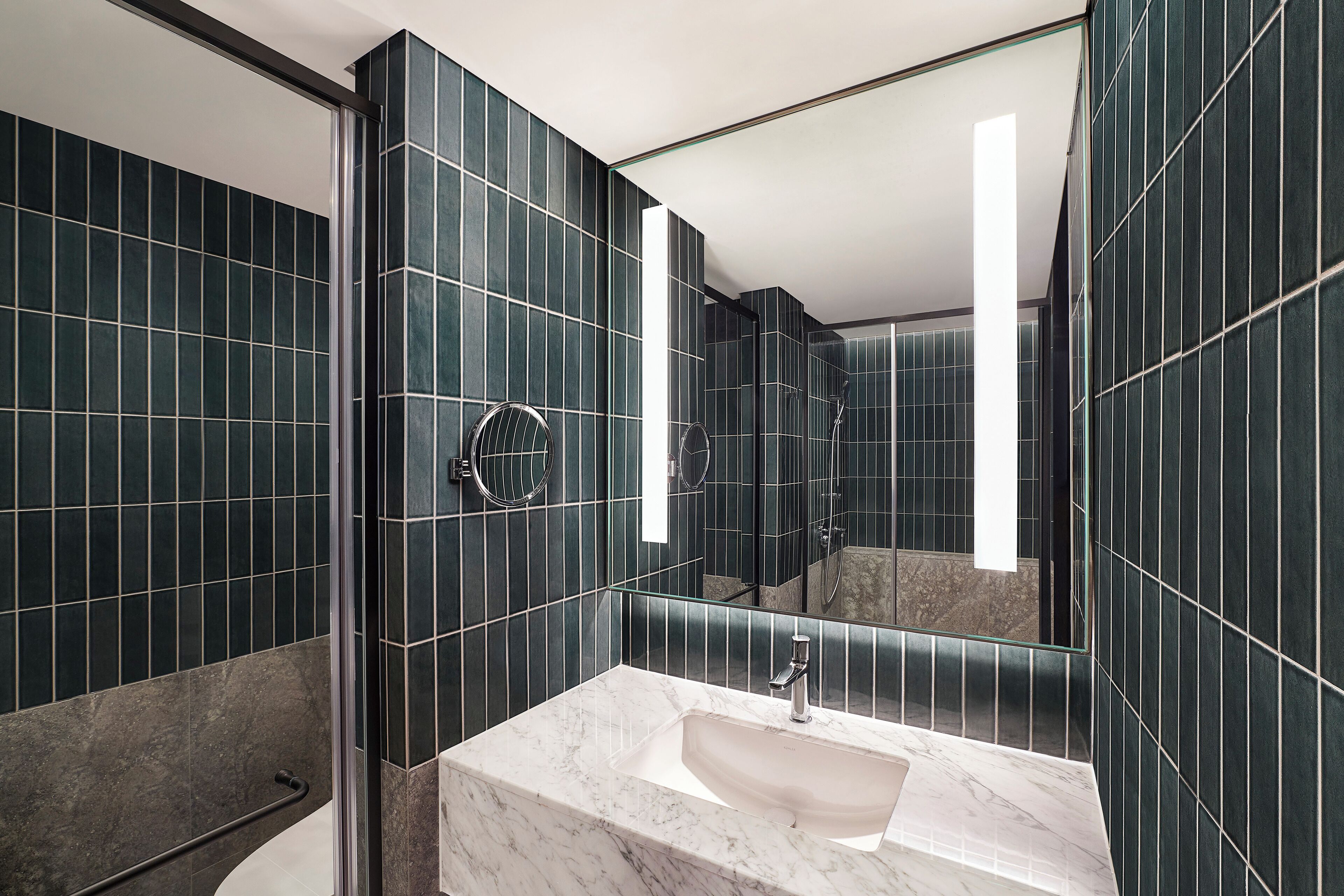 A modern bathroom with dark tiled walls, a marble sink, and a glass shower enclosure.