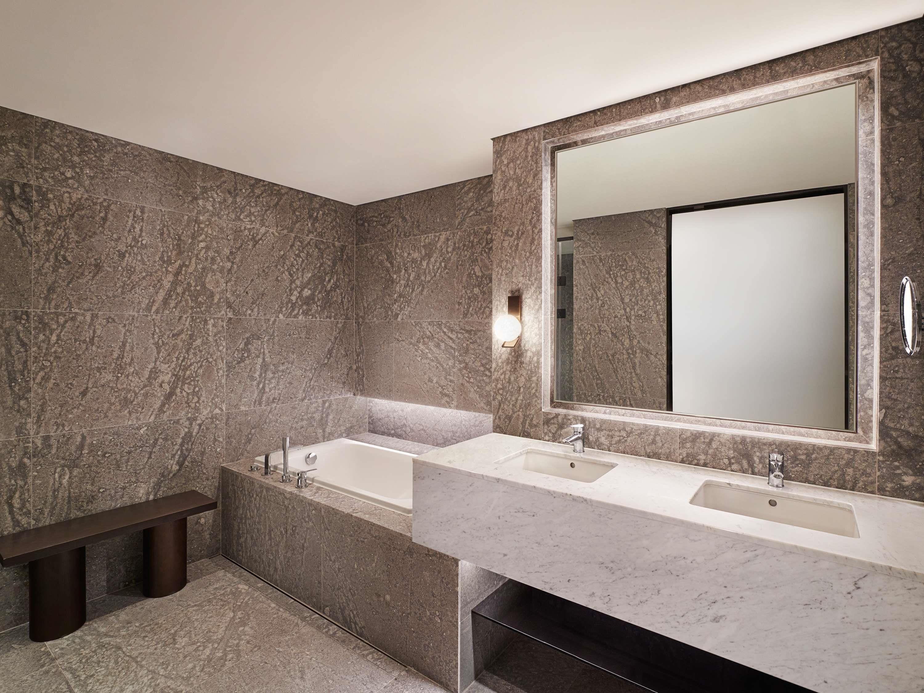 A modern bathroom with a large mirror, two sinks, and a bench.