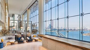 Un vestíbulo amplio con zona de estar, mostrador de recepción y grandes ventanales con vistas a la ciudad.