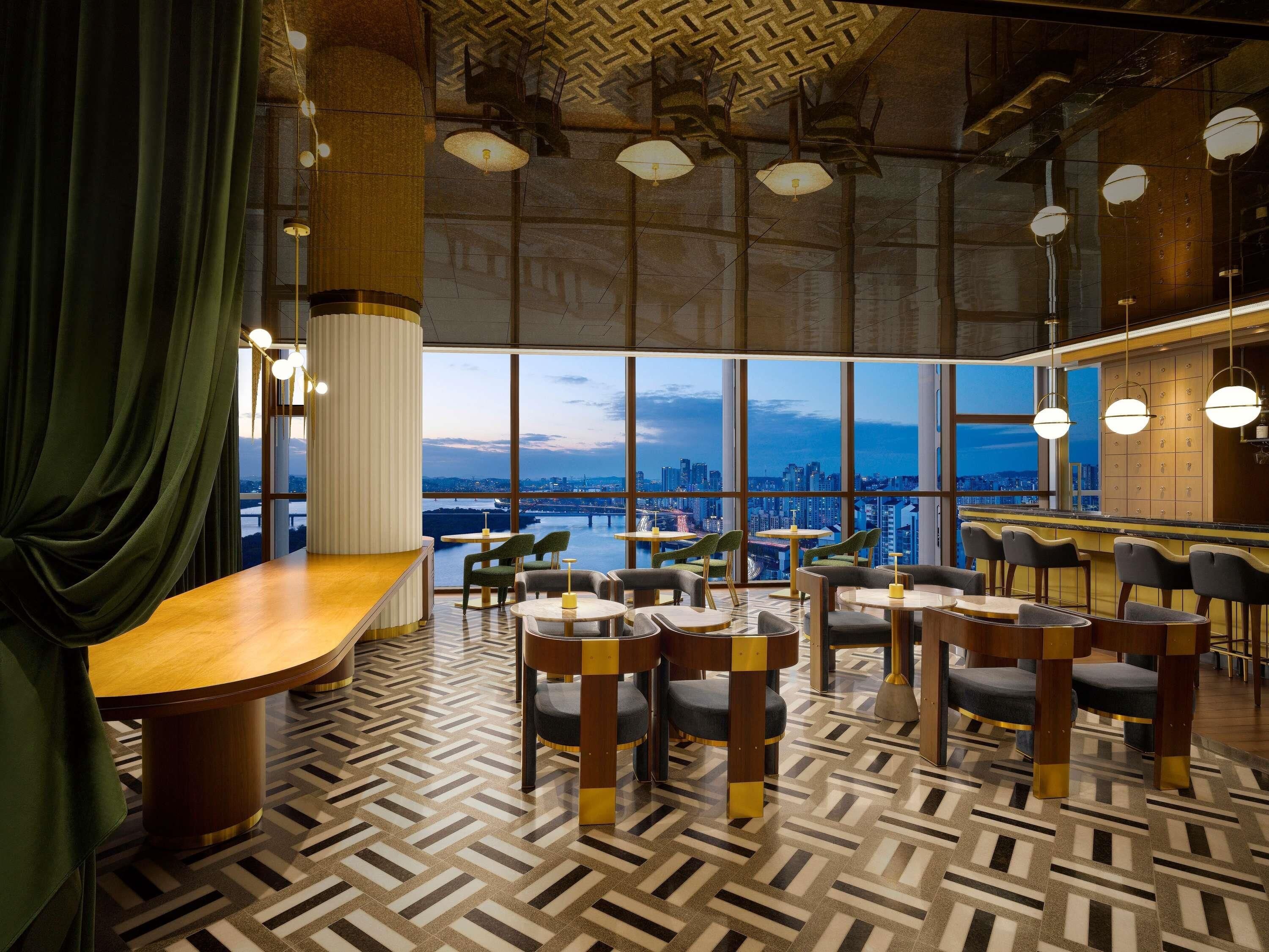 A modern bar area with a panoramic city view, featuring a herringbone floor pattern and contemporary furniture.