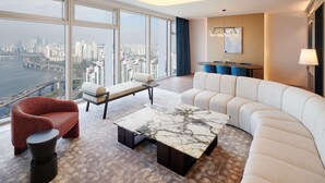 Una sala moderna con un ventanal grande, un sofá, un sillón rojo, una mesa de centro de mármol y una zona de comedor con una mesa y sillas.