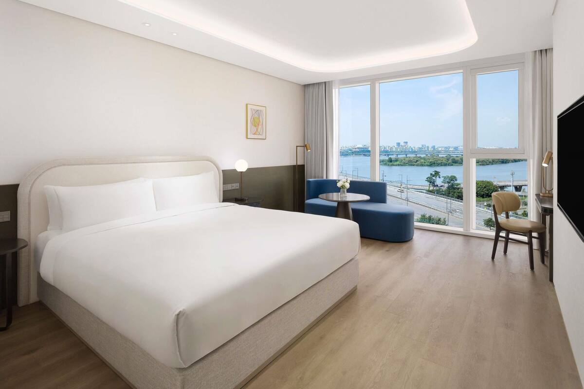 A hotel room with a large bed, a seating area with a view of the city, and a desk with a lamp.