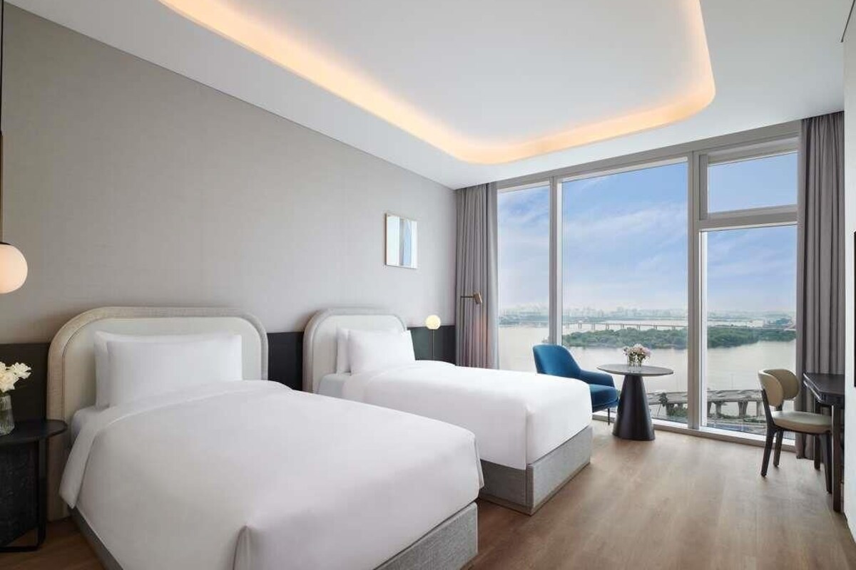 A hotel room with two beds, a dining area, and a large window with a view.