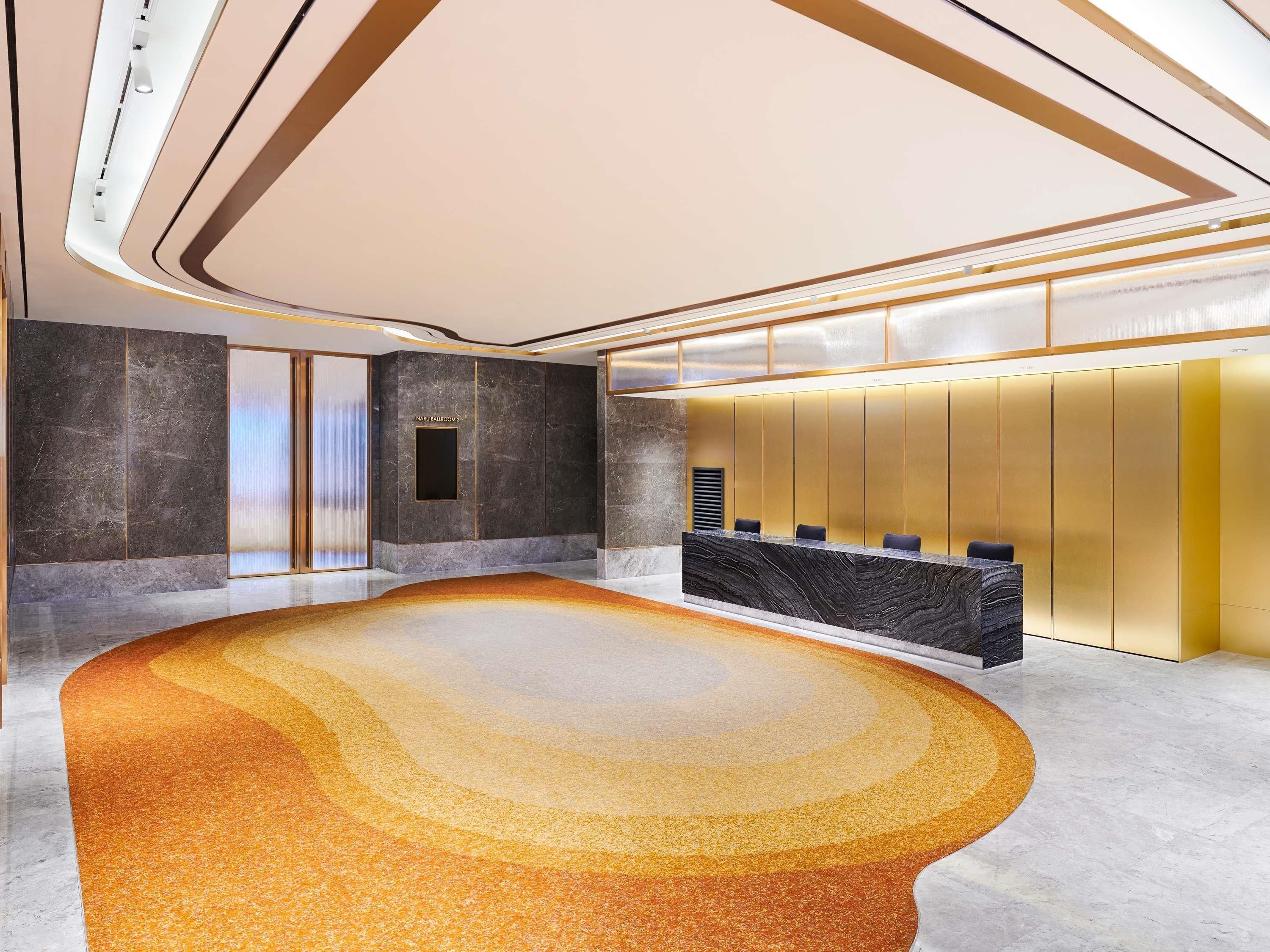 A modern lobby with a marble reception desk, a seating area, and a large wall with a vertical panel design.