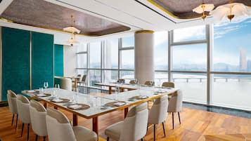 A modern dining area with a large table, chairs, and large windows offering a city view.