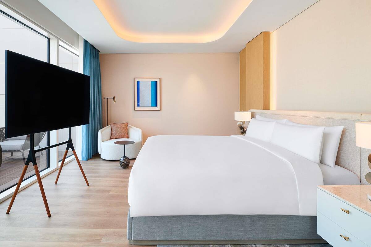 A modern hotel room with a large bed, a flat-screen TV, a small round table, and a chair.