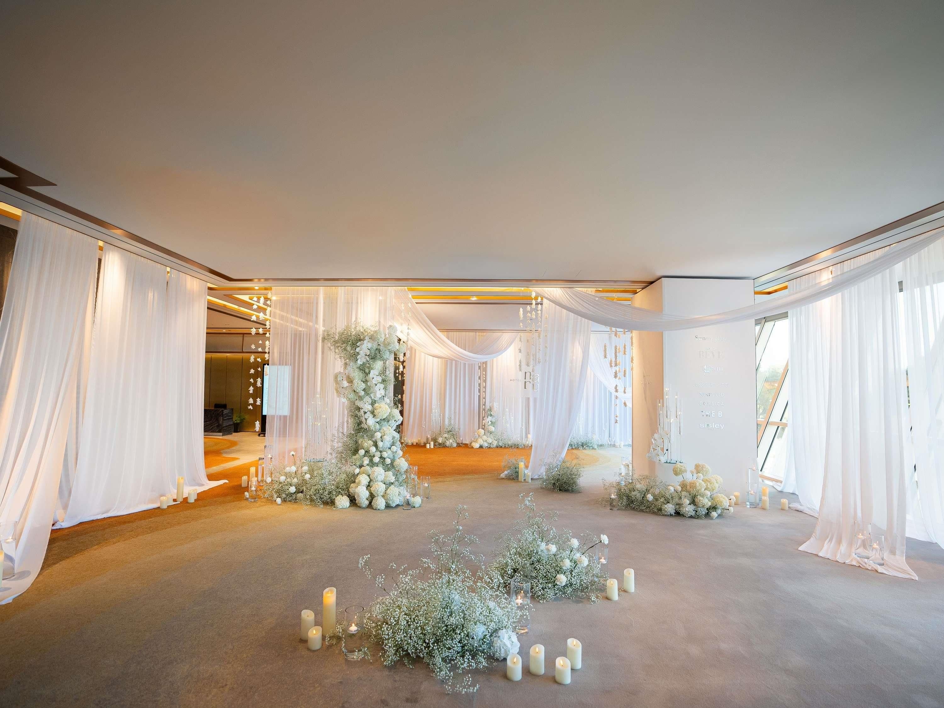 A spacious indoor venue with a carpeted floor, draped curtains, and floral arrangements.