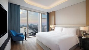 A modern hotel room with a large bed, a blue armchair, a small table with a vase, and a city view through large windows. - Hotel Naru Seoul - MGallery Collection (Seoul)
