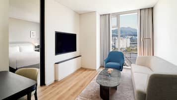 Quarto de hotel moderno com cama, TV, sofá, mesa de centro e vista para a cidade.