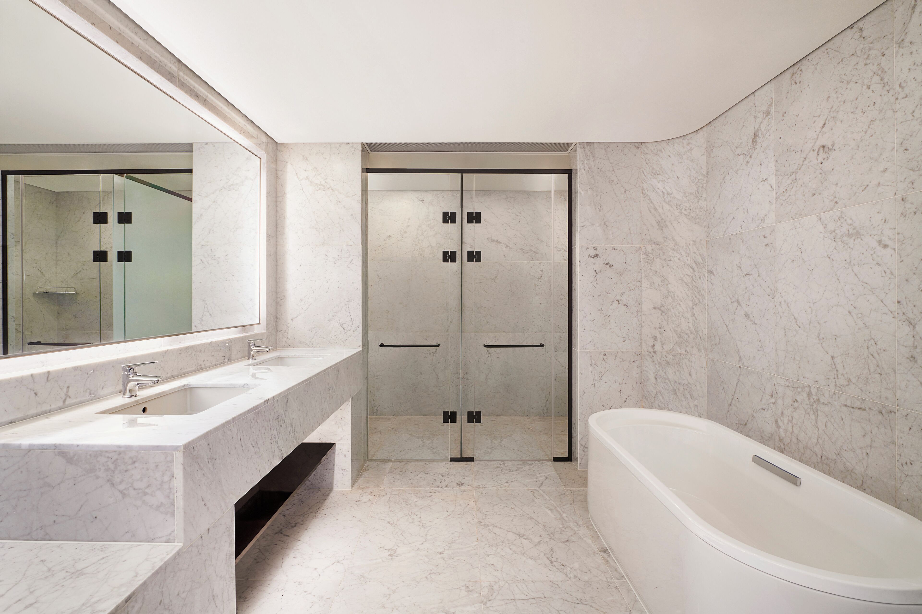 A modern bathroom with a large mirror, two sinks, a bathtub, and a glass-enclosed shower.
