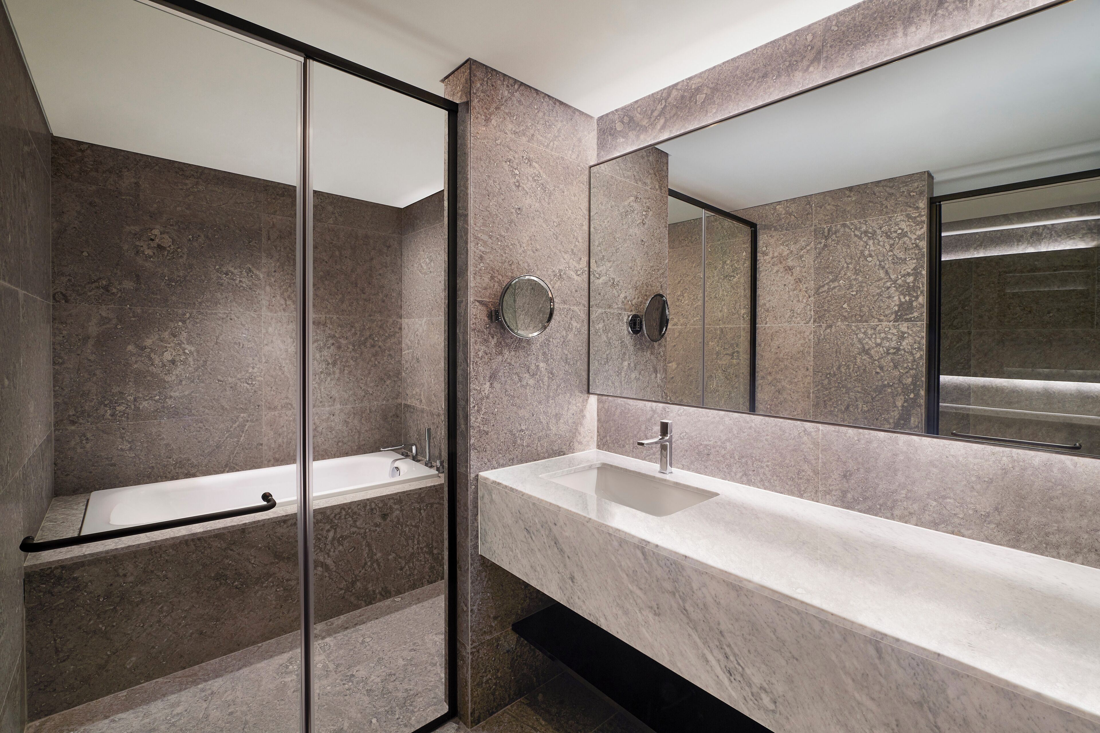 Une salle de bain moderne avec une douche à parois de verre, un grand miroir et un plan de toilette en marbre.