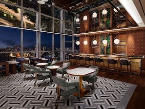 Un bar moderno con techos altos y amplias ventanas que ofrecen vistas a la ciudad.