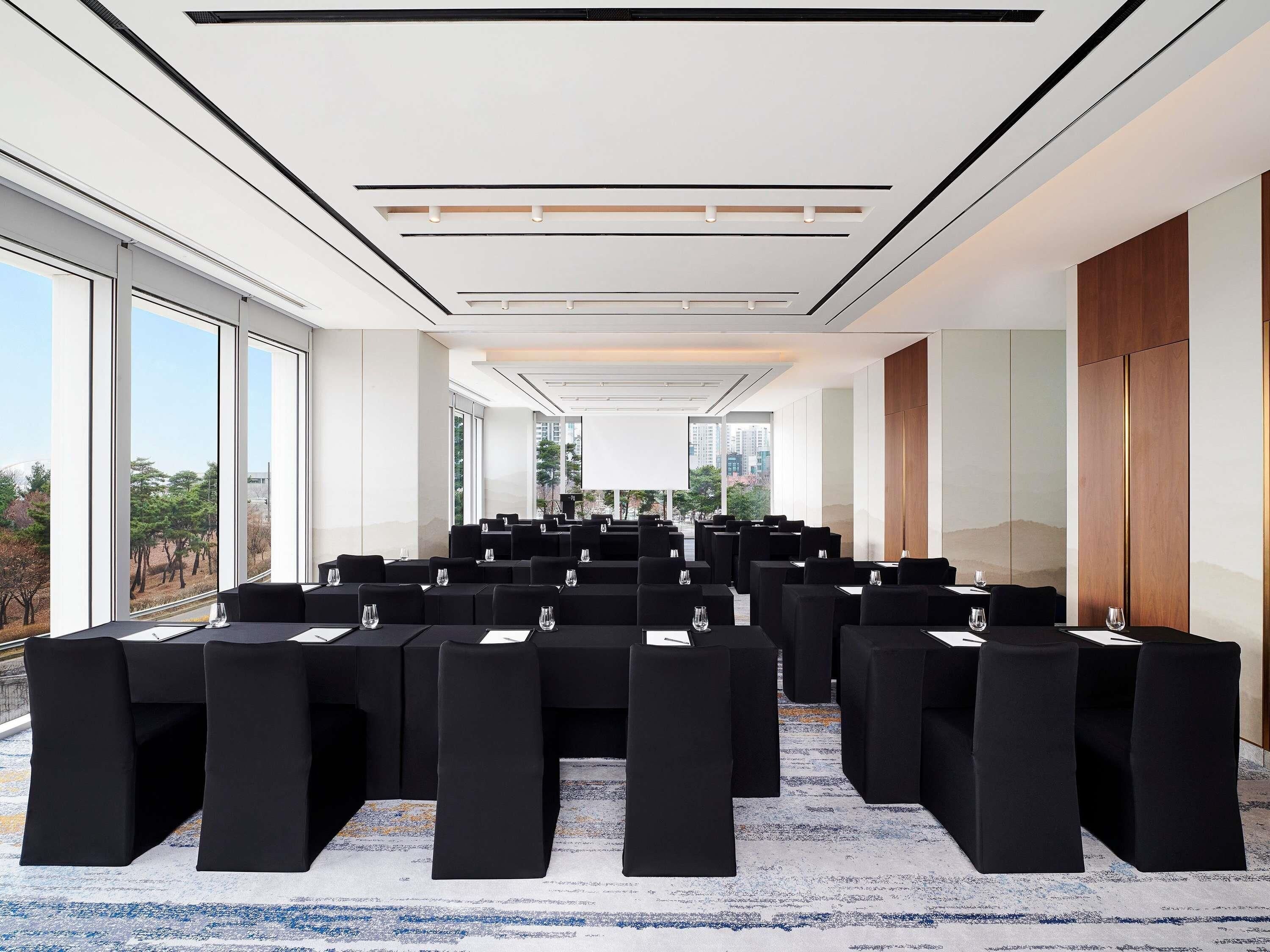 A conference room with rows of tables and chairs, large windows, and a modern ceiling design.