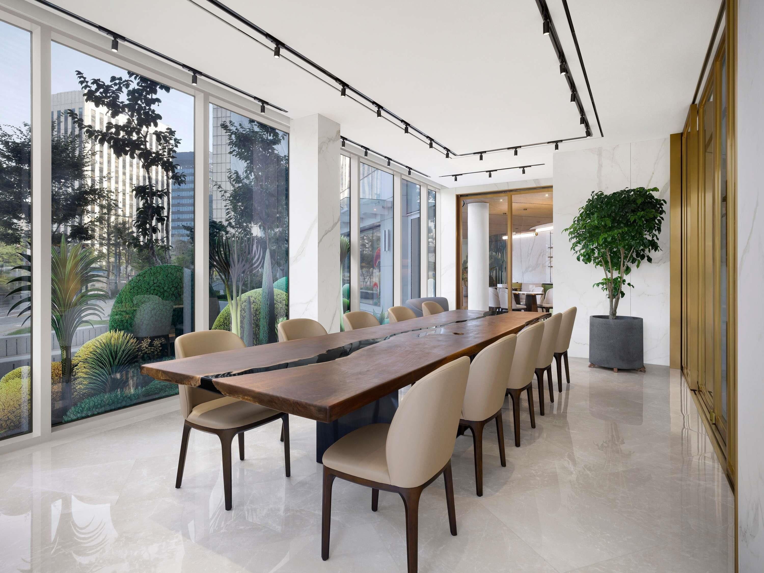 Une salle de conférence moderne, dotée d’une longue table, de chaises et de grandes fenêtres offrant une vue sur la verdure et les bâtiments.
