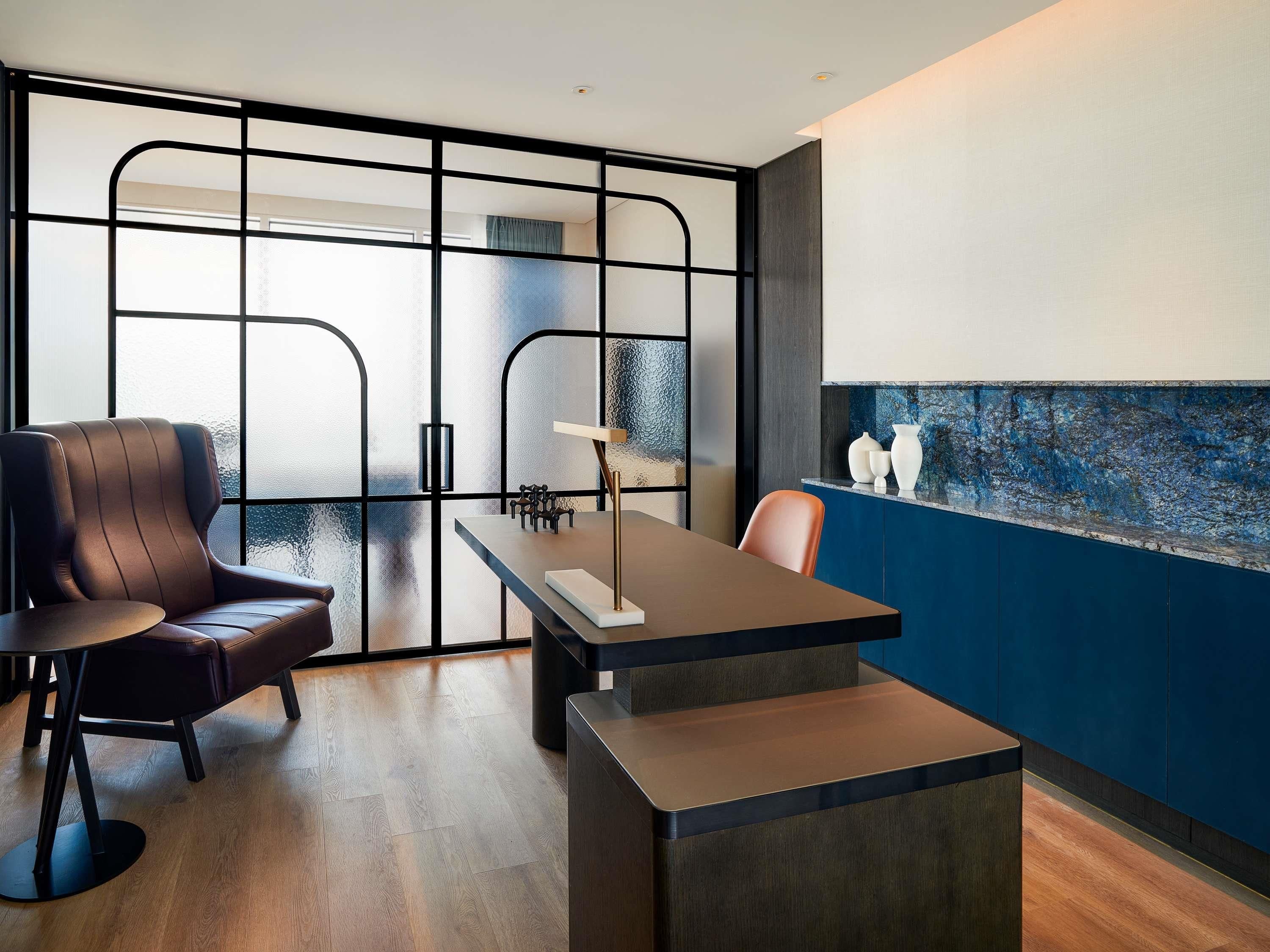 A modern room with a wooden floor, a brown leather chair, a wooden table, and a blue accent wall.