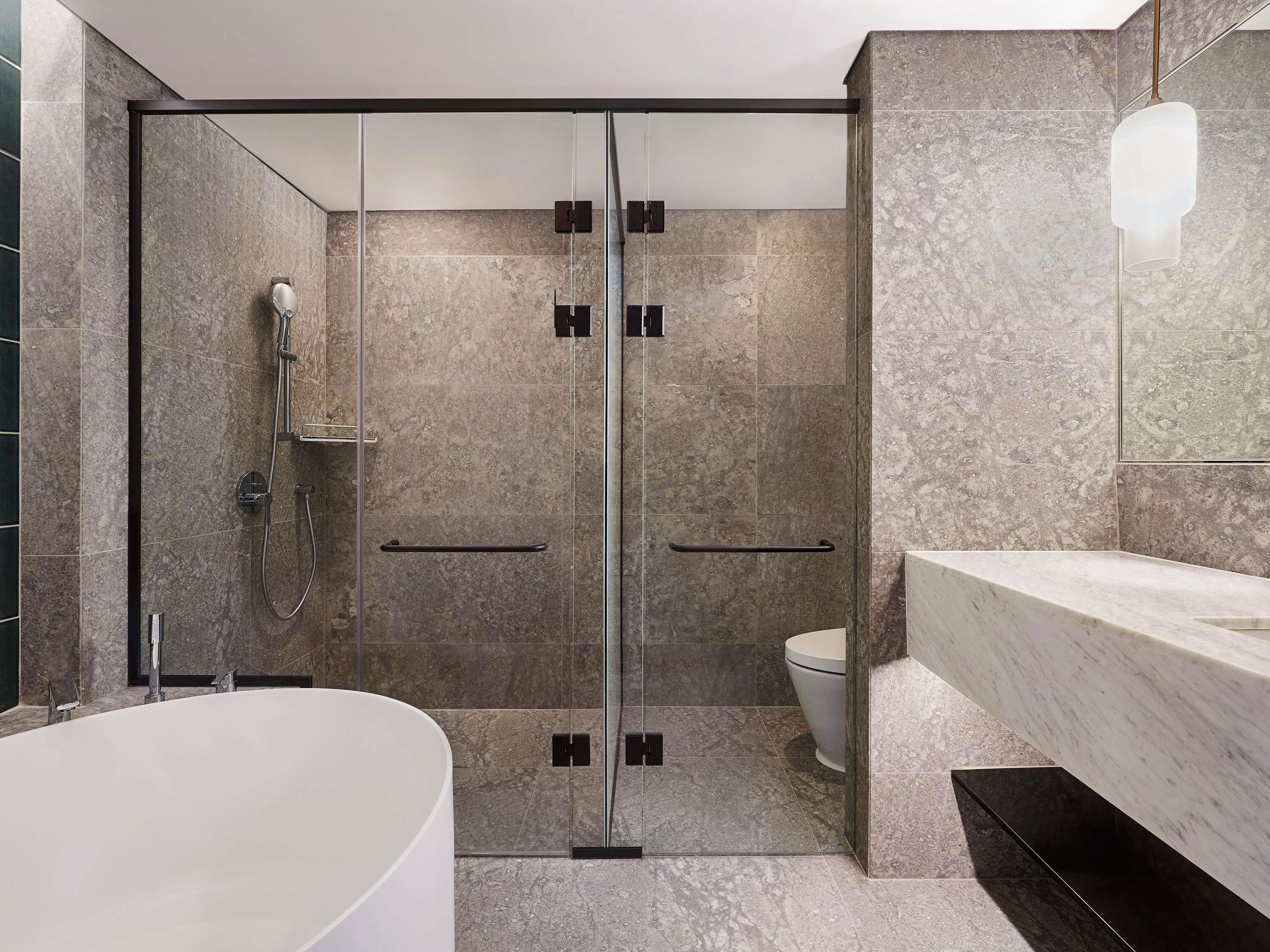 A modern bathroom with a glass-enclosed shower, a white bathtub, and a marble countertop.