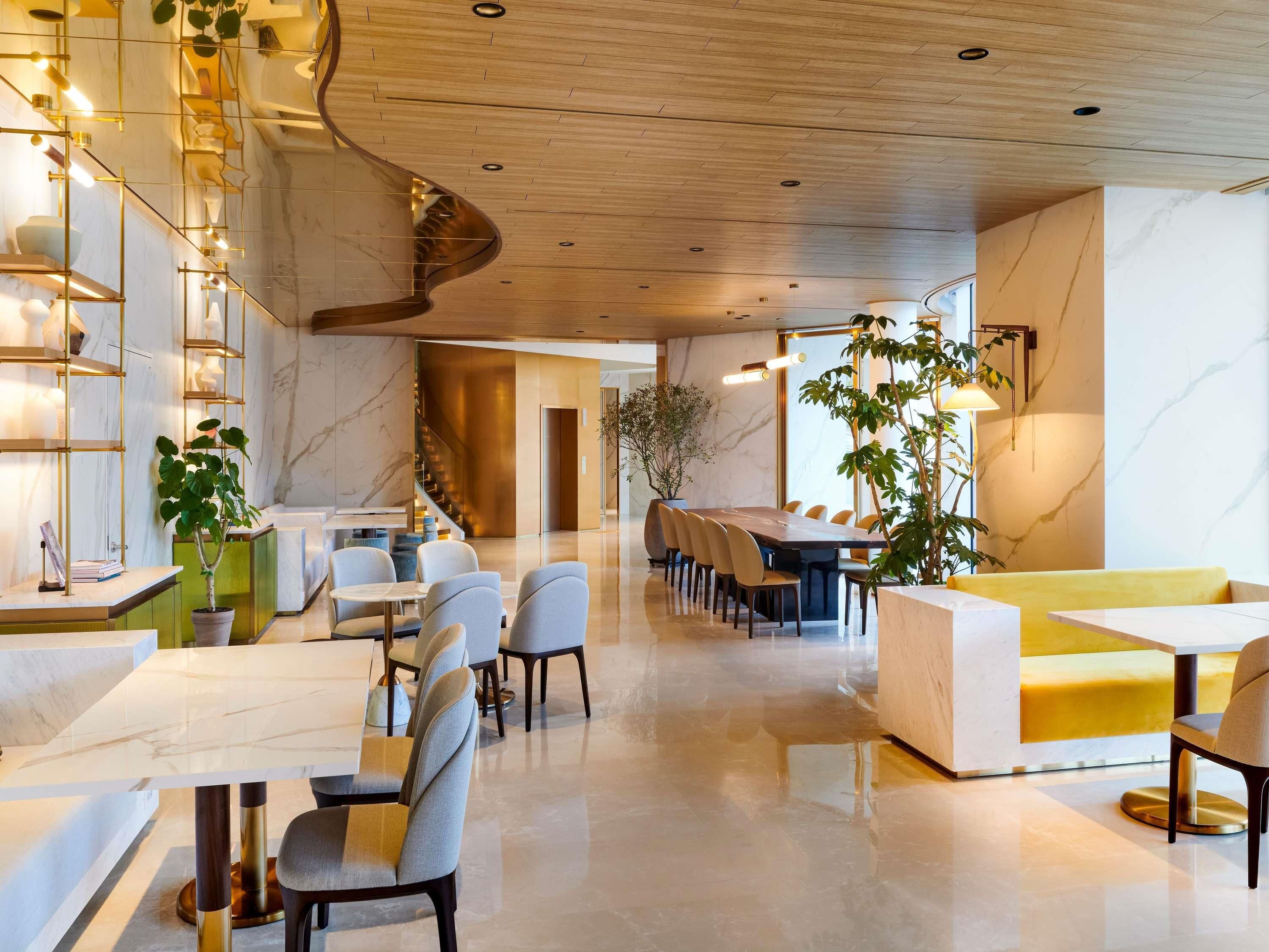 A modern hotel lobby with marble flooring, a reception desk, seating area, and a staircase.