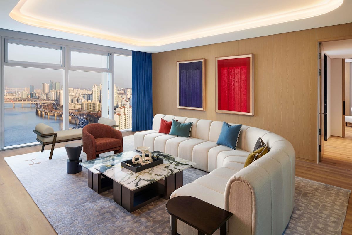A modern living room with a large sofa, a coffee table, and a view of a cityscape through large windows.