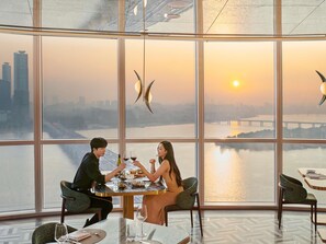 Comedor con amplia ventana que ofrece vista a un paisaje urbano y un río al atardecer.