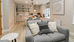 A modern living room with a grey sofa, a small white table, and a kitchen in the background. - Coniston (Kendal)
