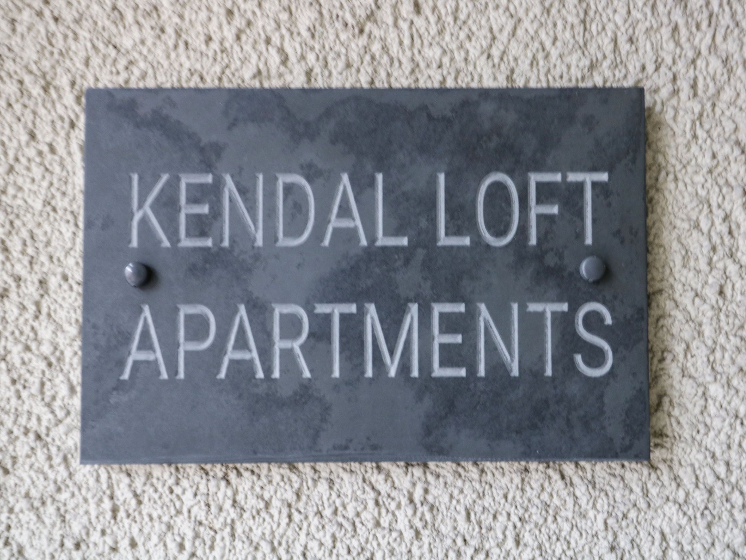 A sign for 'Kendal Loft Apartments' with a simple, dark background and white lettering.