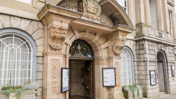 A historic building entrance with ornate stone carvings, a red carpet, and two informational boards. - Coniston (Kendal)
