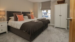 A bedroom with a bed, bedside tables, a wardrobe, and a window with a view of buildings. - Coniston (Kendal)