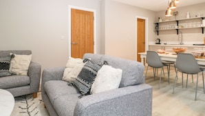 A modern living room with grey sofas, a coffee table, and a kitchen area with a dining table and chairs. - Coniston (Kendal)