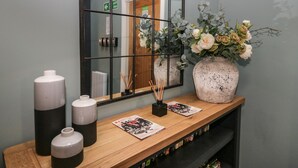 A wooden console table with a large mirror, a vase with flowers, and two candle holders. - Coniston (Kendal)