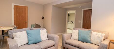 A modern living room with two grey sofas, a coffee table, and a dining area with a table and chairs.