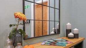Un espace d’accueil avec un comptoir en bois, un miroir, un vase avec une fleur, une citrouille et une étagère contenant des livres et des bouteilles.