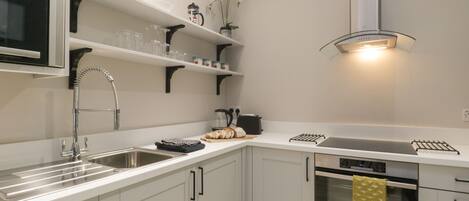 A modern kitchen with white cabinetry, a stainless steel sink, a microwave, a kettle, and a toaster.