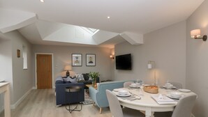 Un salon moderne comprenant un coin repas, un ensemble de canapés, un téléviseur fixé au mur et une lucarne au-dessus de l’espace détente.