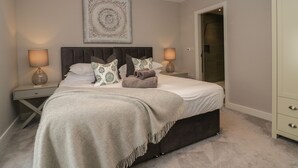 Une chambre à coucher avec un grand lit, deux tables de chevet, une commode, une tête de lit, une œuvre d’art accrochée au mur et une armoire.