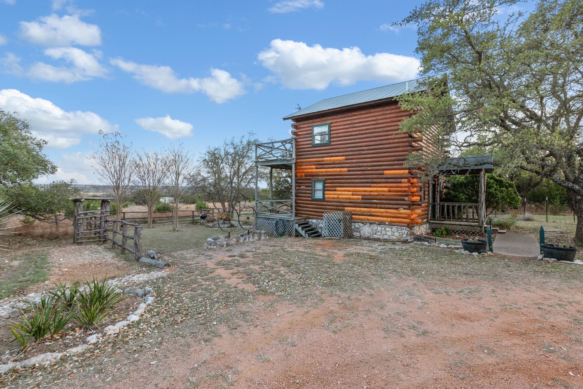 Eine rustikale Blockhütte mit einer Metalltreppe, die zu einer Veranda führt, umgeben von spärlicher Vegetation und einem klaren Himmel.
