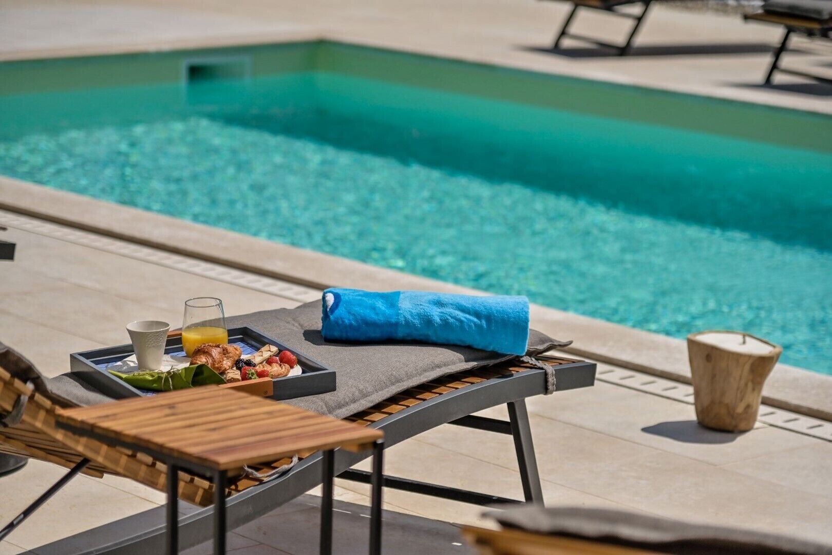 Un coin détente au bord de la piscine avec un transat, un plateau contenant des articles pour le petit-déjeuner et une serviette bleue.