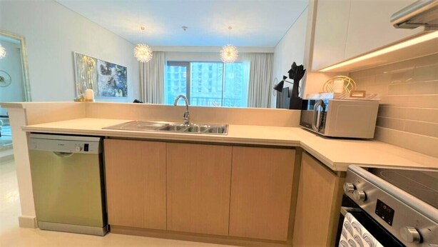 A modern kitchen with a built-in dishwasher, a stainless steel sink, a microwave, and a stove. - Luxury Dubai Creek Harbour Waterfront Apartment (Dubai)