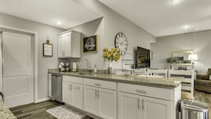 Una cocina moderna con gabinetes blancos, encimeras de granito y lavavajillas integrado.